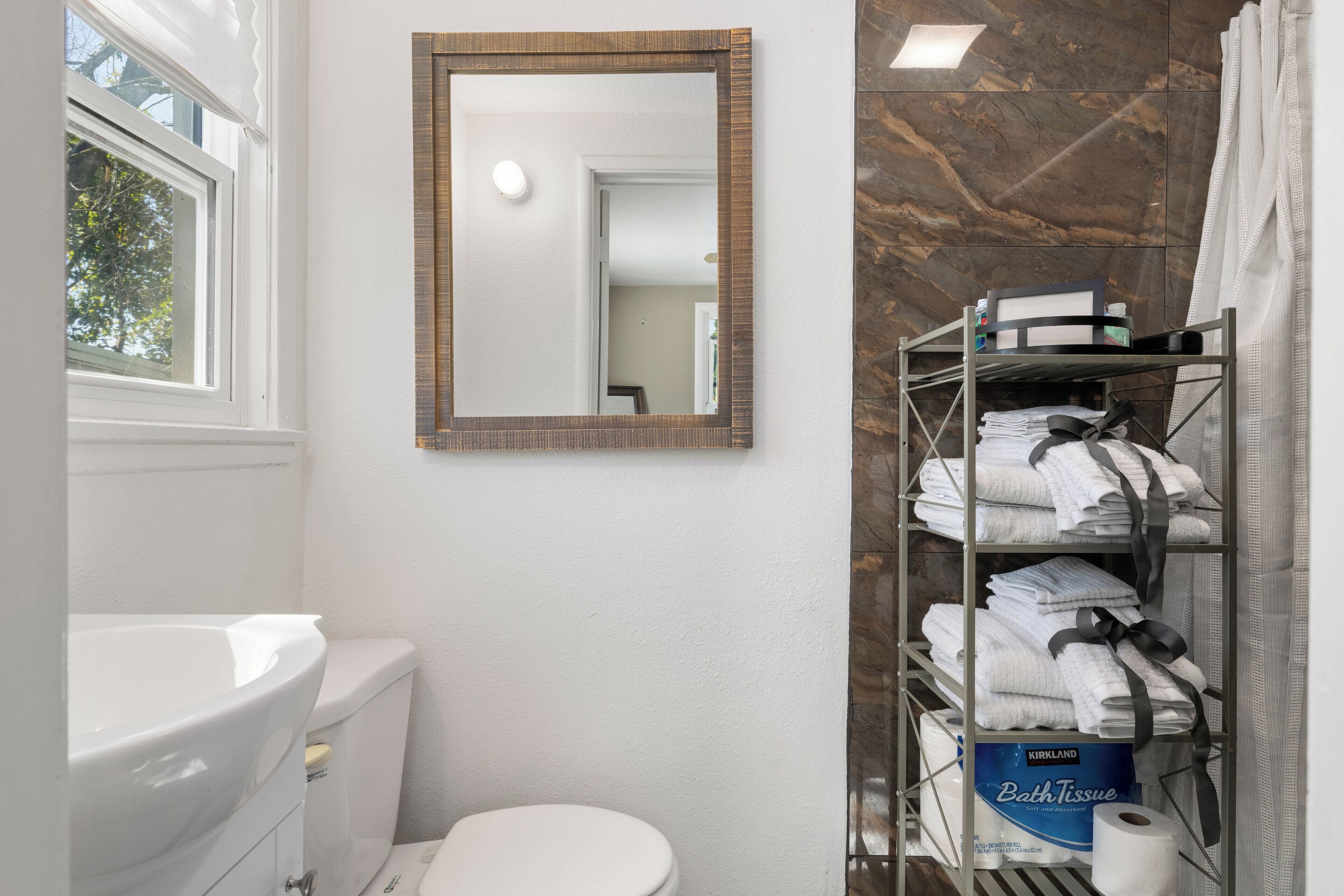 Een badkamer met een wit toilet, een witte wasbak, een spiegel en een plank met handdoeken en wc-papier.