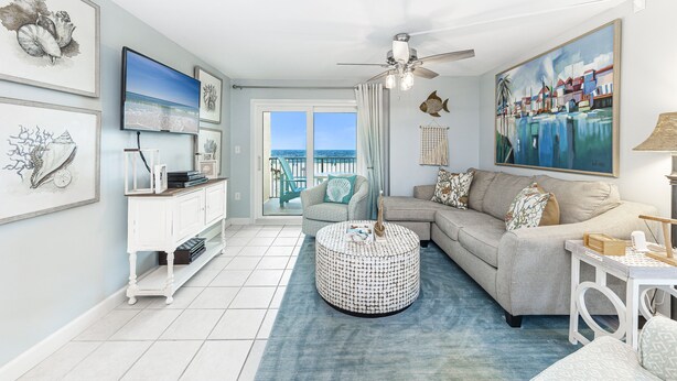 A living room with a large window, a ceiling fan, a round ottoman, and a sofa.