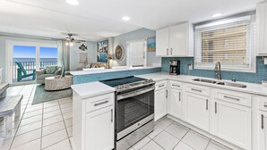 A modern kitchen with white cabinets, a built-in oven, and a large window with blinds.