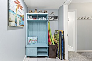 Een blauwe bank met een kussen, een wandplank met decoratieve objecten, en een surfplankhouder.