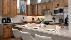 Een moderne keuken met houten kastjes, een centraal eiland met zitplaatsen, roestvrijstalen apparatuur en hanglampen.