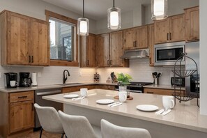 A modern kitchen with wooden cabinets, a central island with seating, stainless steel appliances, and pendant lighting. - Elk Creek A103 private hot tub (Fraser)