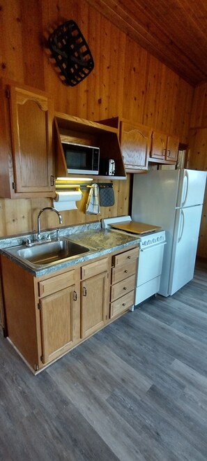 A kitchen with wooden cabinets, a stainless steel sink, a microwave, a stove, and a refrigerator.