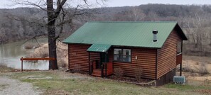 A small log cabin with a green roof, situated by a river.