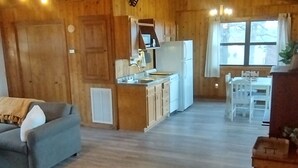 A cozy wooden cabin interior with a living area, kitchen, and dining space.