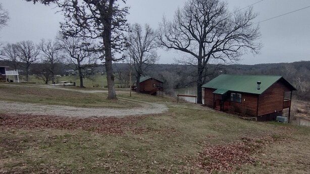 A rural cabin with a green roof, surrounded by trees and a dirt path.