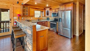 A spacious kitchen with wooden cabinets, granite countertops, a stainless steel refrigerator, and a stone island with bar stools.
