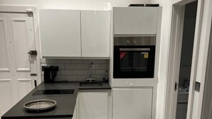 A modern kitchen with white cabinetry, a black countertop, and a marble floor. - Immaculate 1-bed Apartment in the Heart of Chelsea (London)