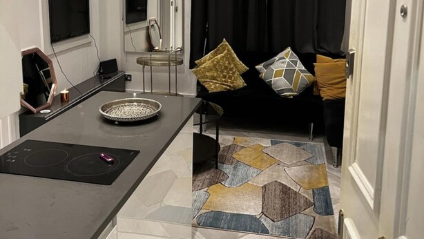 A modern living room with a dining area, a black curtain, a patterned rug, and a marble floor. - Immaculate 1-bed Apartment in the Heart of Chelsea (London)