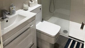 A modern bathroom with a glass-enclosed shower, a white sink, and a toilet. - Immaculate 1-bed Apartment in the Heart of Chelsea (London)