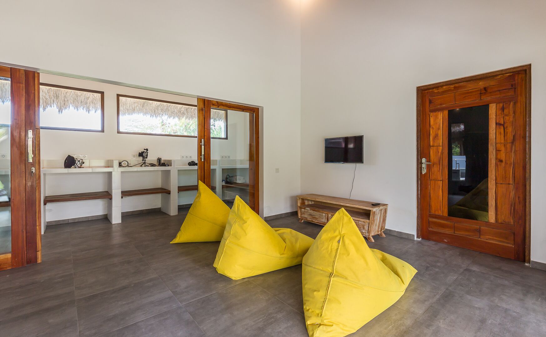 Una habitación moderna con suelo de madera, un televisor fijado a la pared y una puerta de madera.