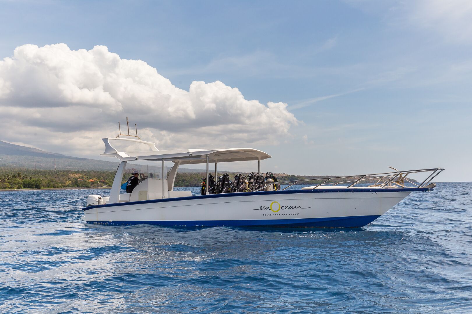 A white and blue boat with 'emOcean' branding, equipped with scuba gear, sailing on calm waters.