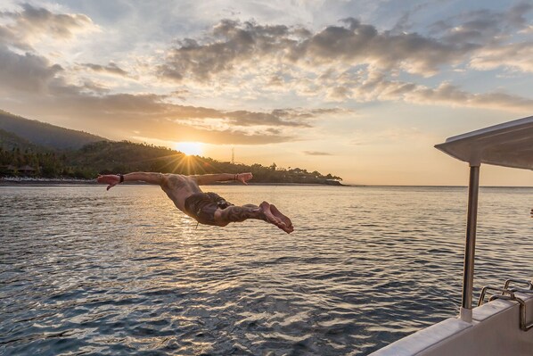Una persona se sumerge en aguas tranquilas al atardecer, con un bote y una costa distante a la vista.