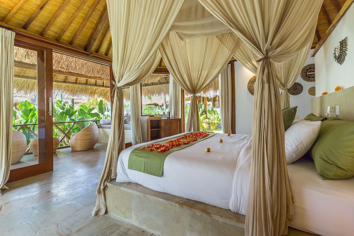 Une pièce avec un lit, des rideaux, un plafond en bois et une vue sur la verdure.