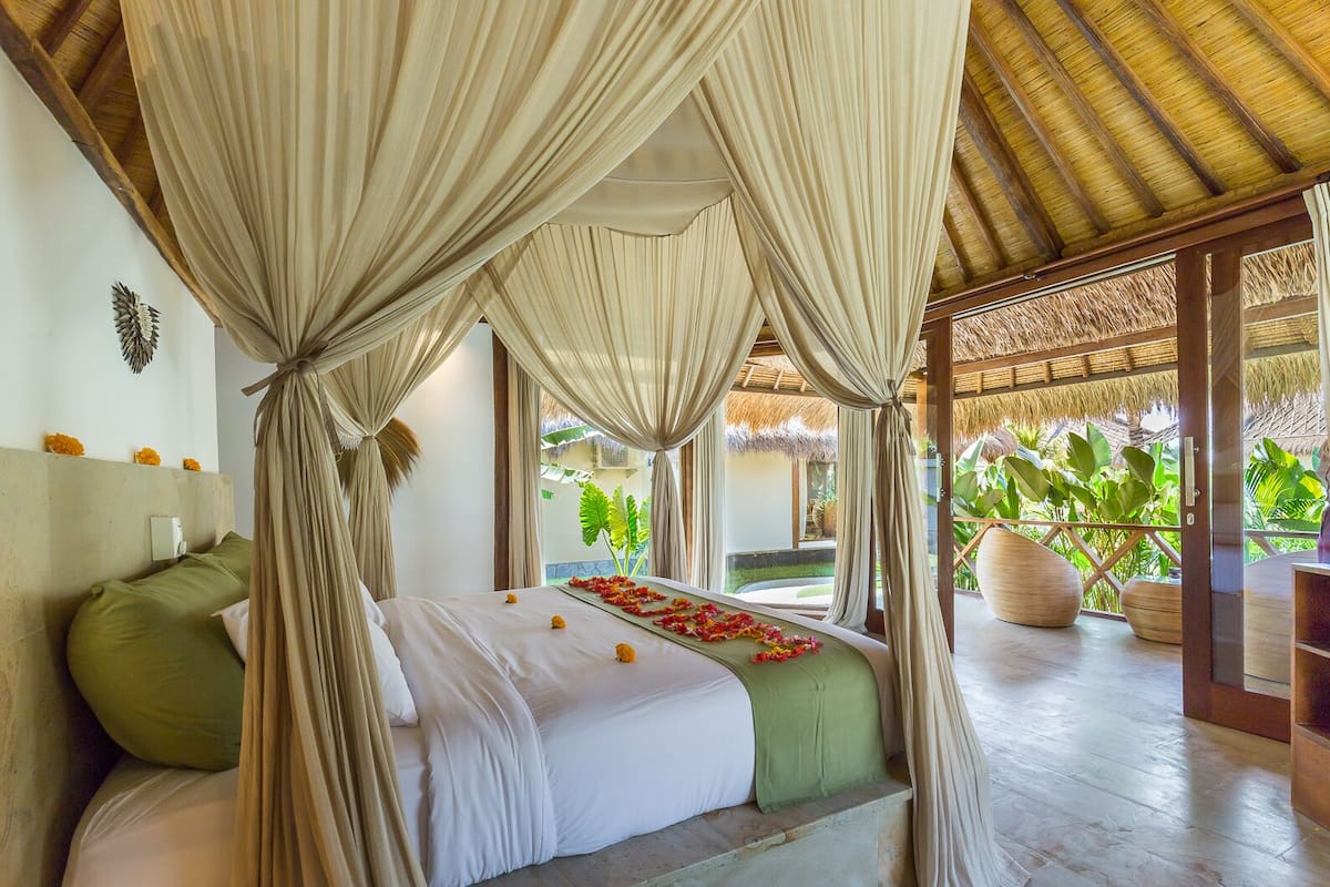 Une chambre avec un lit, des oreillers verts, un baldaquin et une vue sur la verdure.