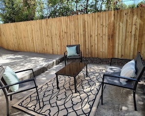 An outdoor seating area with a wooden fence, a patterned rug, and metal chairs.