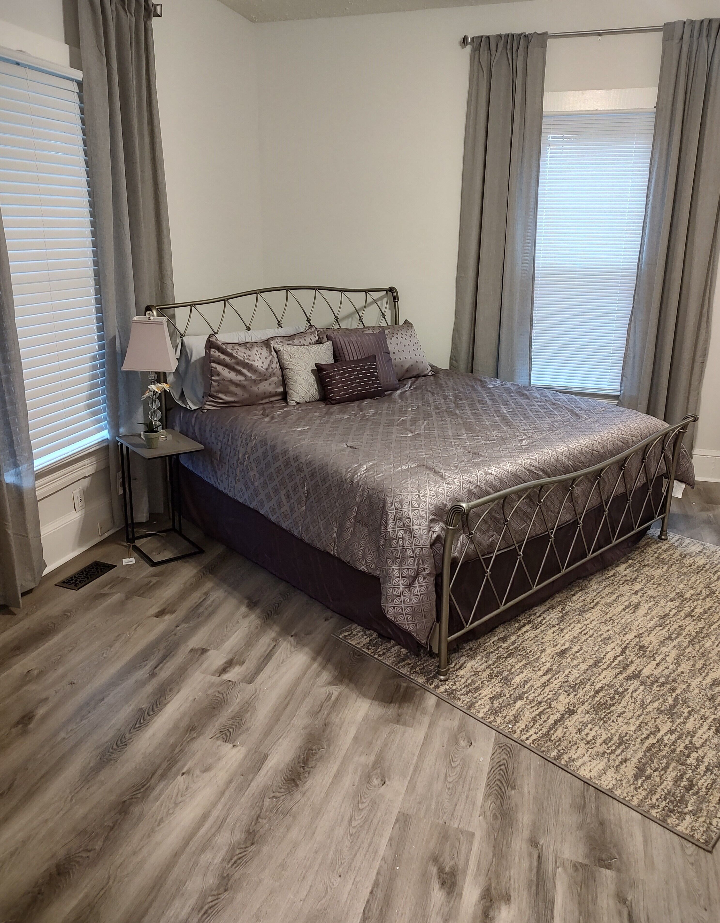 A neatly arranged bedroom with a bed, a bedside table, a lamp, and a window with curtains.