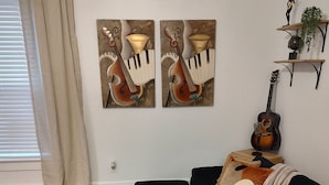 A living room with a dark blue sofa, a wooden coffee table with candles and a plant, and two wall-mounted paintings of musical instruments. - Historic Tootie Frootie House - Within 1 mile of Downtown Macon (Macon)
