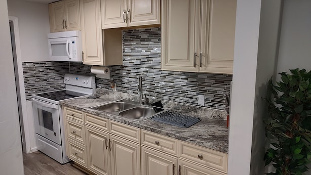 A kitchen with beige cabinets, a stainless steel sink, a microwave, and a tiled backsplash. - Historic Tootie Frootie House - Within 1 mile of Downtown Macon (Macon)
