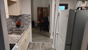 A modern kitchen with a built-in oven, a refrigerator, and a dining area with a table and chairs. - Historic Tootie Frootie House - Within 1 mile of Downtown Macon (Macon)