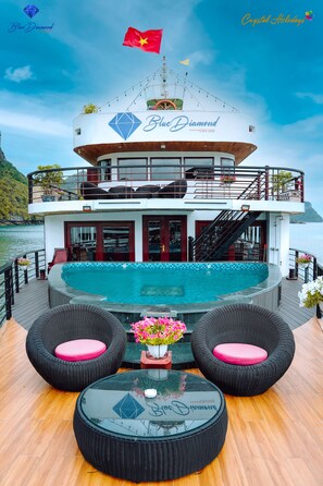 Um navio de cruzeiro com piscina, área externa para sentar e varanda com bandeira.