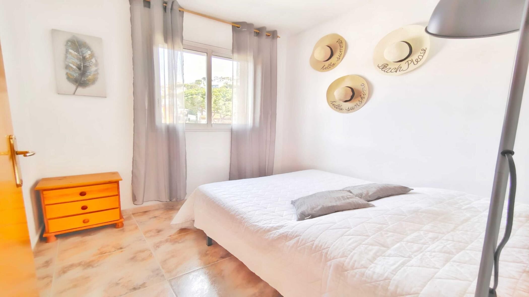 A bedroom with a bed, a nightstand, a window with curtains, and wall decorations.