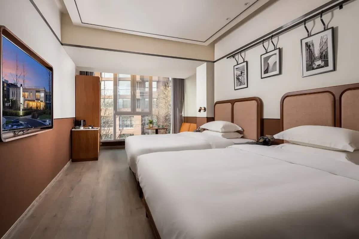 Habitación de hotel con dos camas, un ventanal grande y un televisor de pantalla plana.