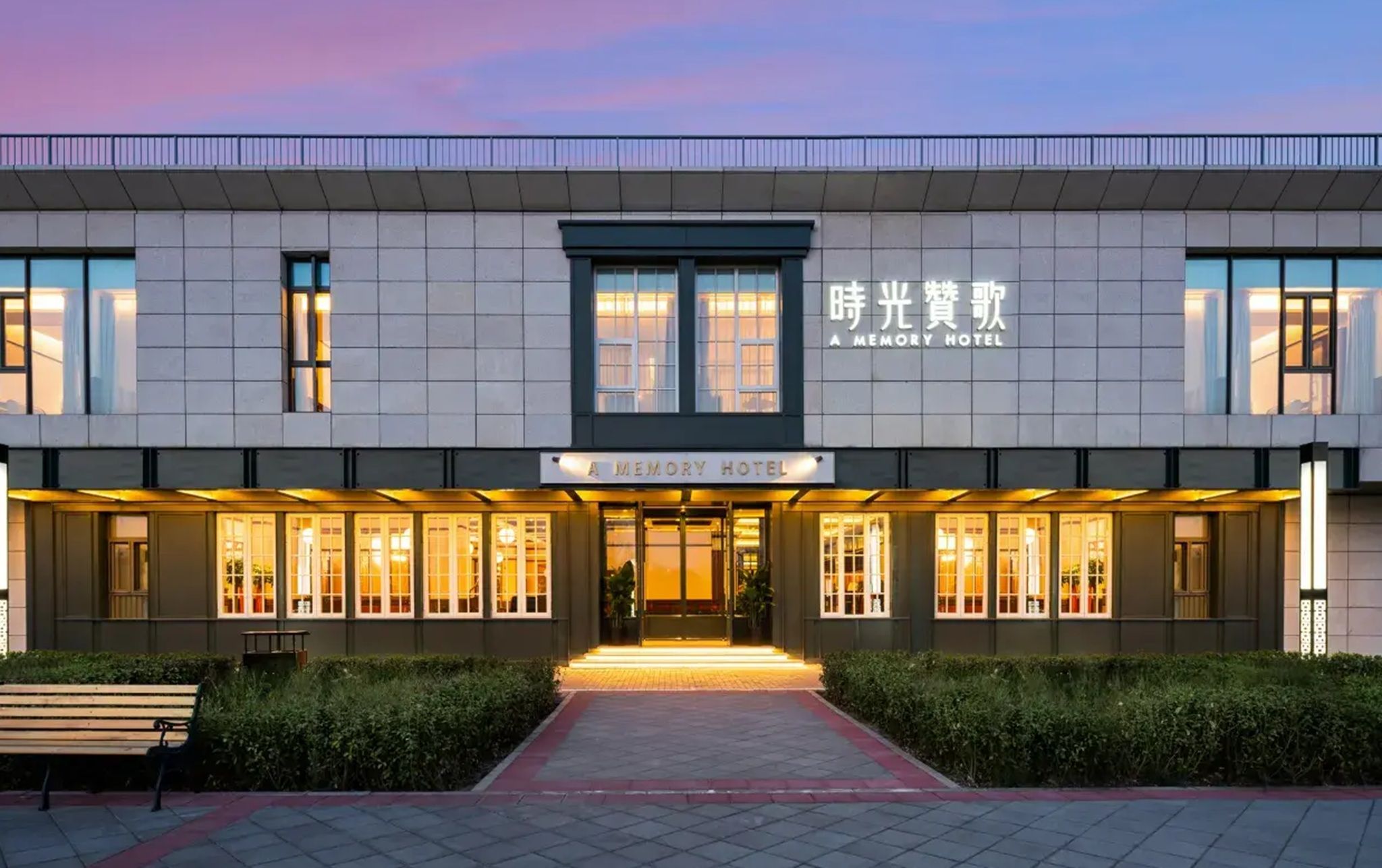Un hôtel moderne, avec une enseigne indiquant « A MEMORY HOTEL », et une grande entrée avec un chemin menant aux portes.