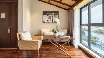 Una habitación con piso de madera, un sofá, una silla, una mesa con una planta, un cuadro en la pared y un ventanal con vistas.