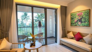 A room with a sofa, chairs, a small table with a vase, and a balcony with a view of palm trees.