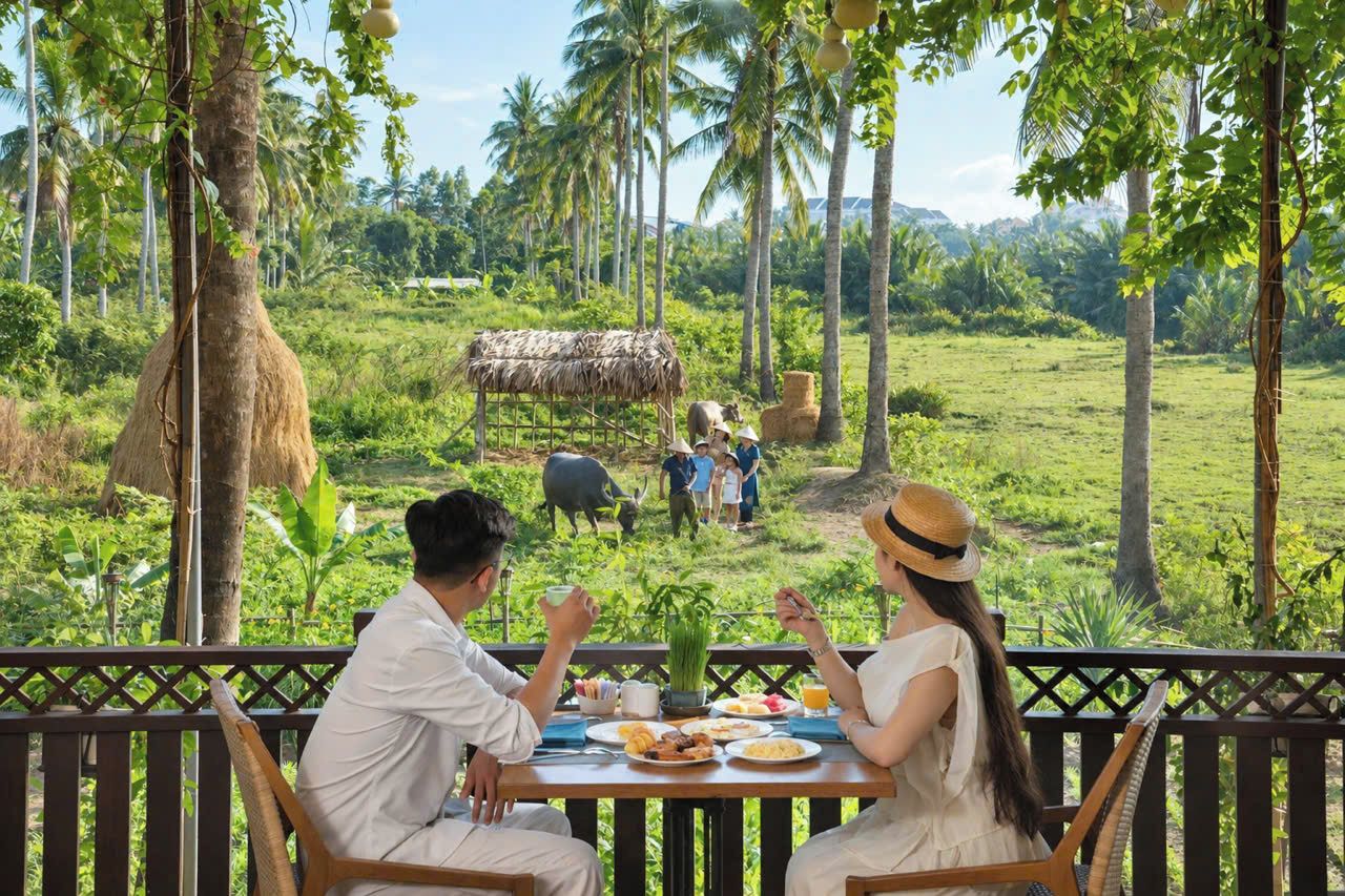 Un comedor con vista a un paisaje rural, que incluye una estructura con techo de paja y una vaca al fondo.