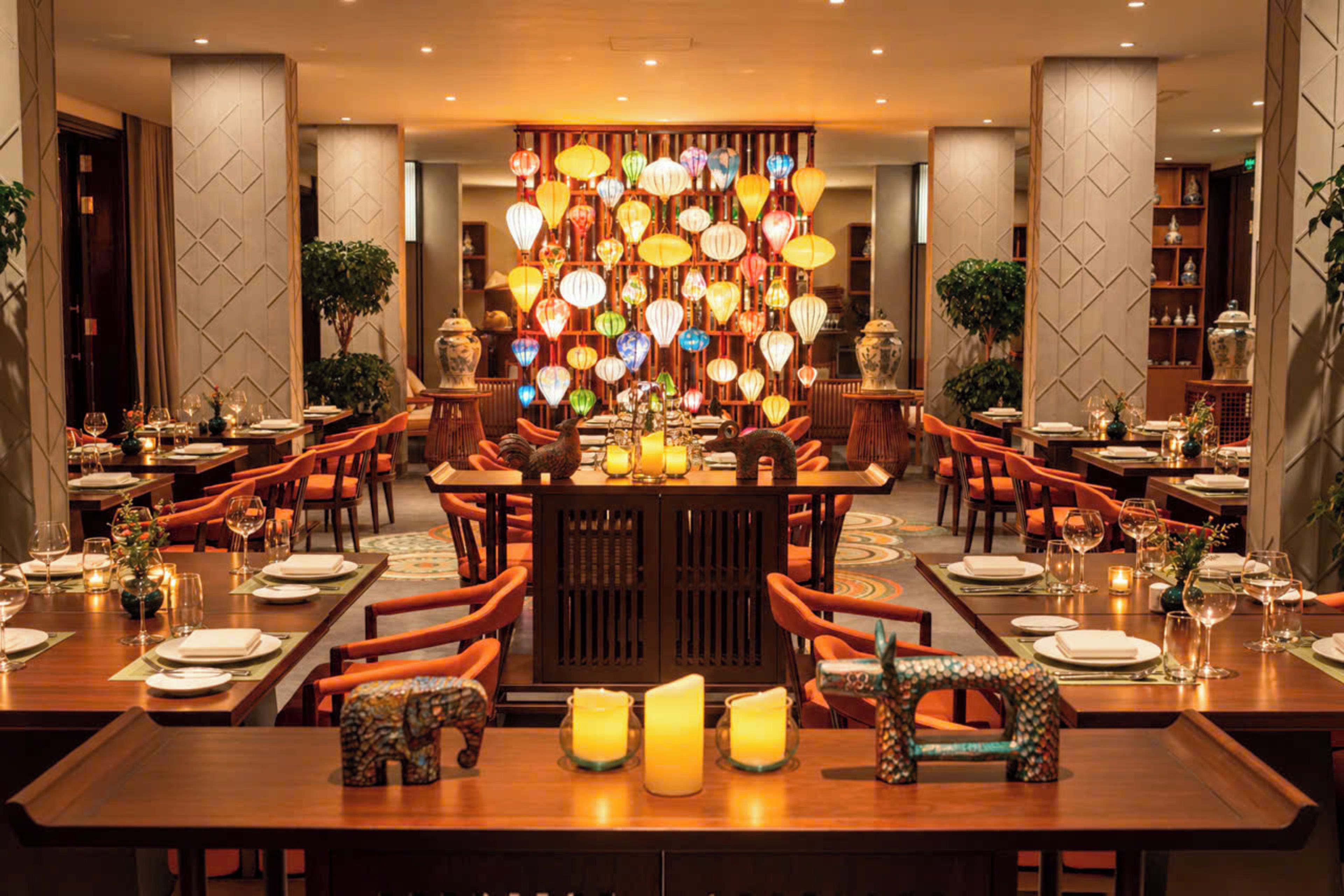 A restaurant with multiple dining tables, orange chairs, and a decorative wall with hanging lanterns.
