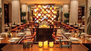 A restaurant with multiple dining tables, orange chairs, and a decorative wall with hanging lanterns.