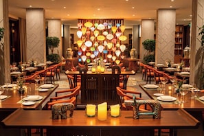 Un restaurant doté de plusieurs tables, de chaises orange et d’un mur décoratif orné de lanternes suspendues.