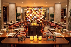 Un restaurante con varias mesas, sillas color naranja y una pared decorativa con faroles colgantes.