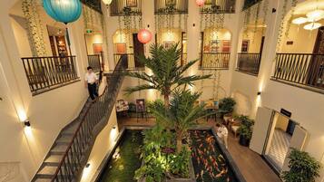 Un vestíbulo de hotel con una fuente central, varios balcones y plantas de interior.