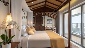 A bedroom with a large bed, a bedside lamp, a potted plant, and a view of the balcony.