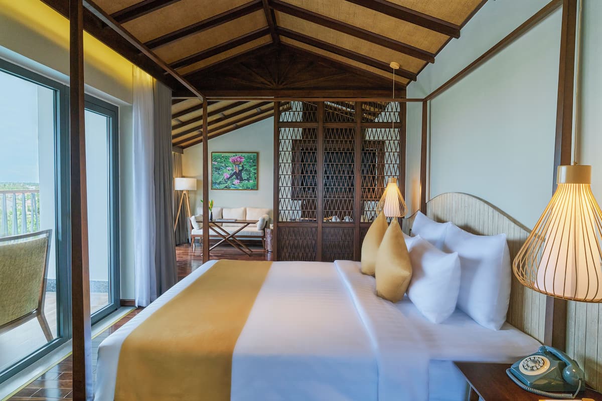 Une chambre d’hôtel avec un grand lit, un plafond en bois, une vue sur l’extérieur, une petite table avec une lampe et un tableau au mur.