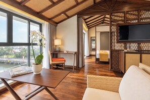 Une chambre d’hôtel avec un plancher en bois, un coin repas avec une table et des chaises, un canapé, un téléviseur et une vue sur un pont et l’eau à l’extérieur.