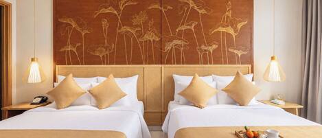 A hotel room with two beds, a wooden headboard with floral carvings, bedside lamps, and a tray with fruit and a cup on the bed.