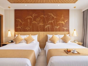 Een hotelkamer met twee bedden, een houten hoofdbord met bloemdecoraties, nachtlampjes en een dienblad met fruit en een beker op het bed.