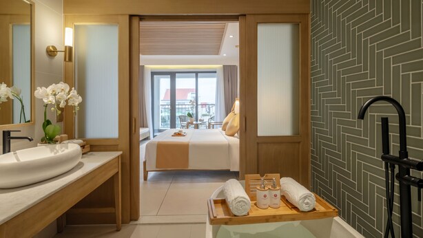 A modern hotel bathroom with a large sink, a wooden vanity, a bathtub, and a shower area.