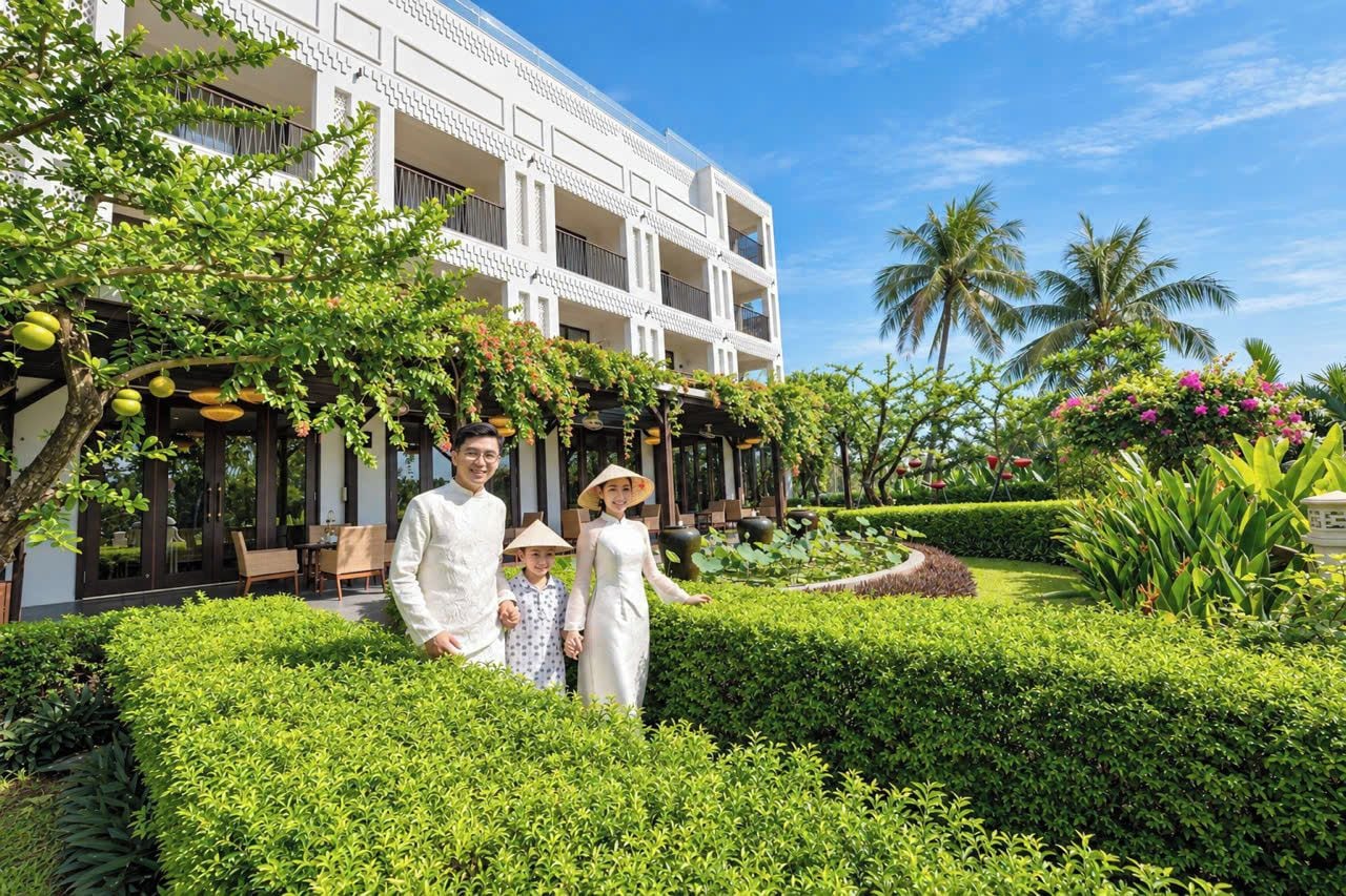 Una familia vestida con atuendo tradicional posa en un jardín cuidado, con un edificio moderno al fondo.