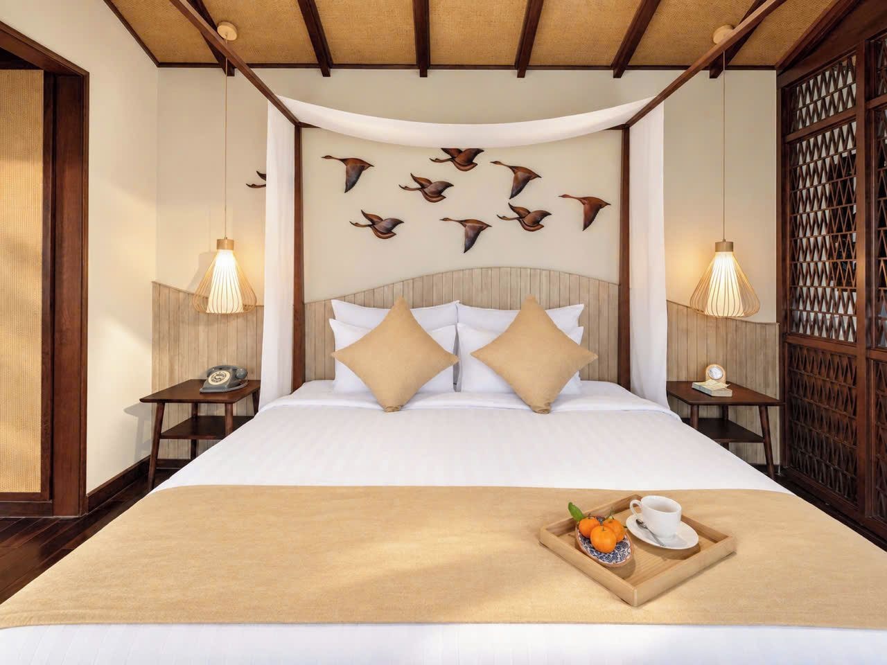 A hotel room with a bed, two bedside tables, a wall-mounted telephone, and a tray with a cup and fruit.