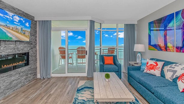 A modern living room with a fireplace, a sofa, a coffee table, and a balcony with ocean views. - Carolinian 931 (Myrtle Beach)