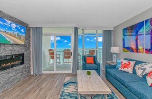 A modern living room with a fireplace, a sofa, a coffee table, and a balcony with ocean views.