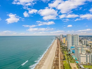 A coastal cityscape with a beach, high-rise buildings, and a clear sky.