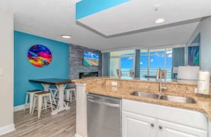 A modern kitchen with granite countertops, a dishwasher, and a dining area with bar stools.