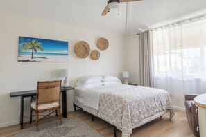 Une chambre à coucher avec un lit, une chaise, un bureau, une lampe et un tableau représentant une scène de plage.