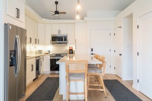 Een moderne keuken met witte kastjes, roestvrijstalen apparatuur, een centraal eiland met zitplaatsen en een plafondventilator.